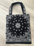 Black tote bag with white bandana pattern on a light wooden surface